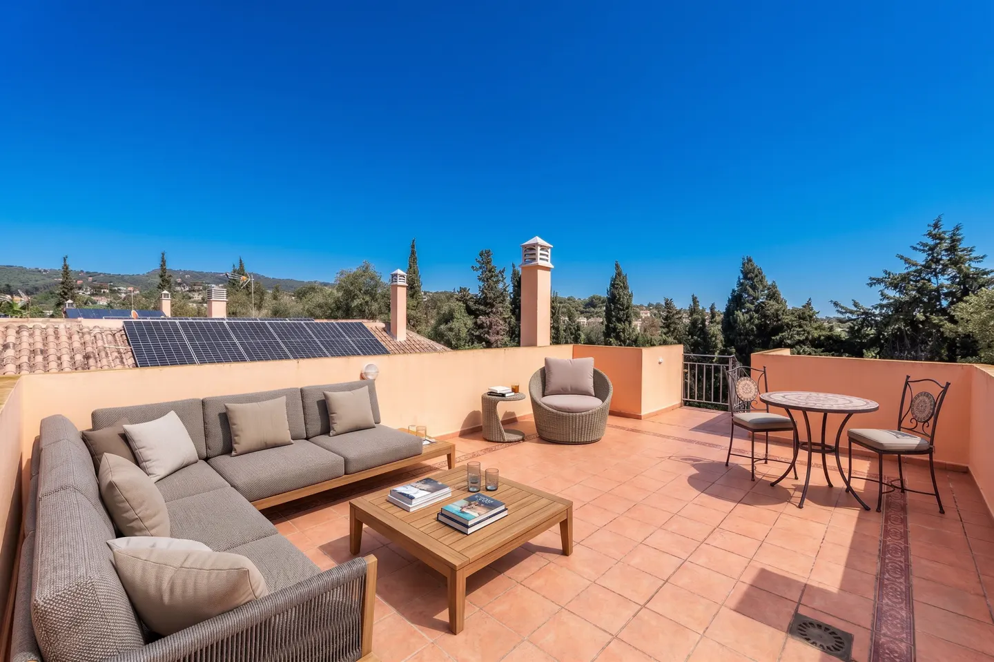 Outdoor patio with terracotta tiles, gray wicker furniture, and a table set for two against a clear blue sky.
