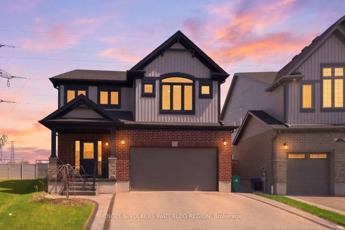 Two-story house with gray siding, brick accents, and a two-car garage at dusk.