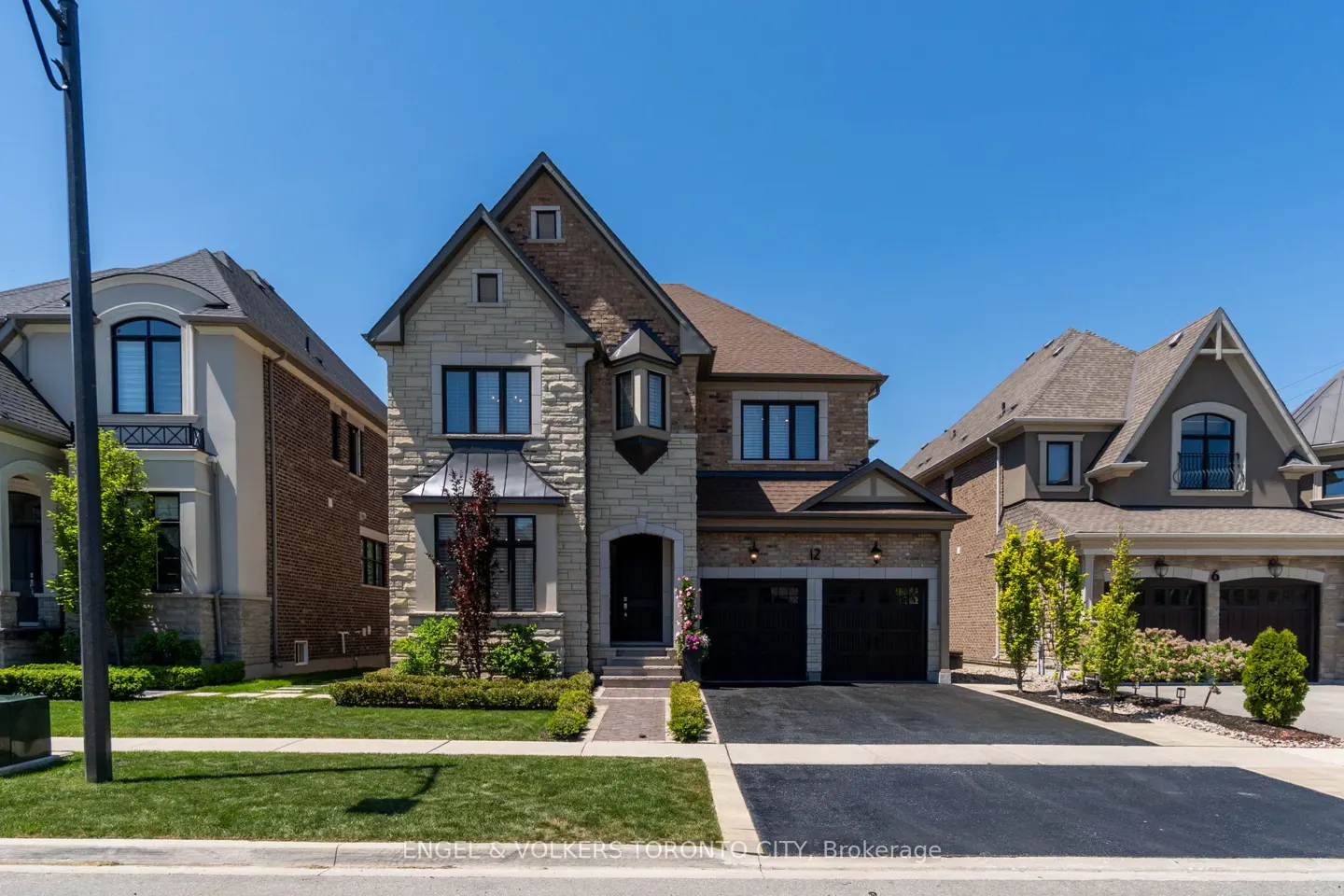 Two-story stone and brick suburban home with a double garage, manicured lawn, and clear blue sky.