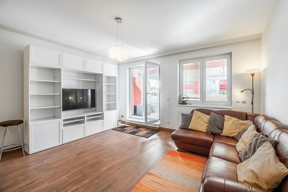 Modern living room with a brown leather sectional, white wall unit, TV, and orange area rug on wood-look tile flooring. [AI-generated text]