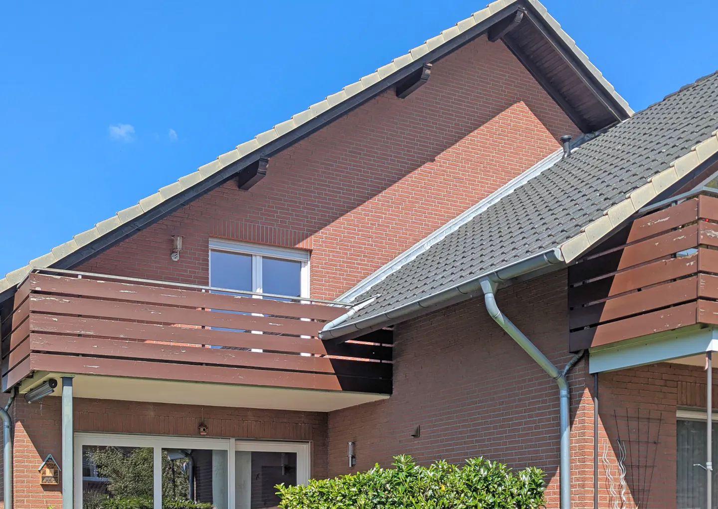 A two-story brick house with a brown balcony and a gray tiled roof under a blue sky.