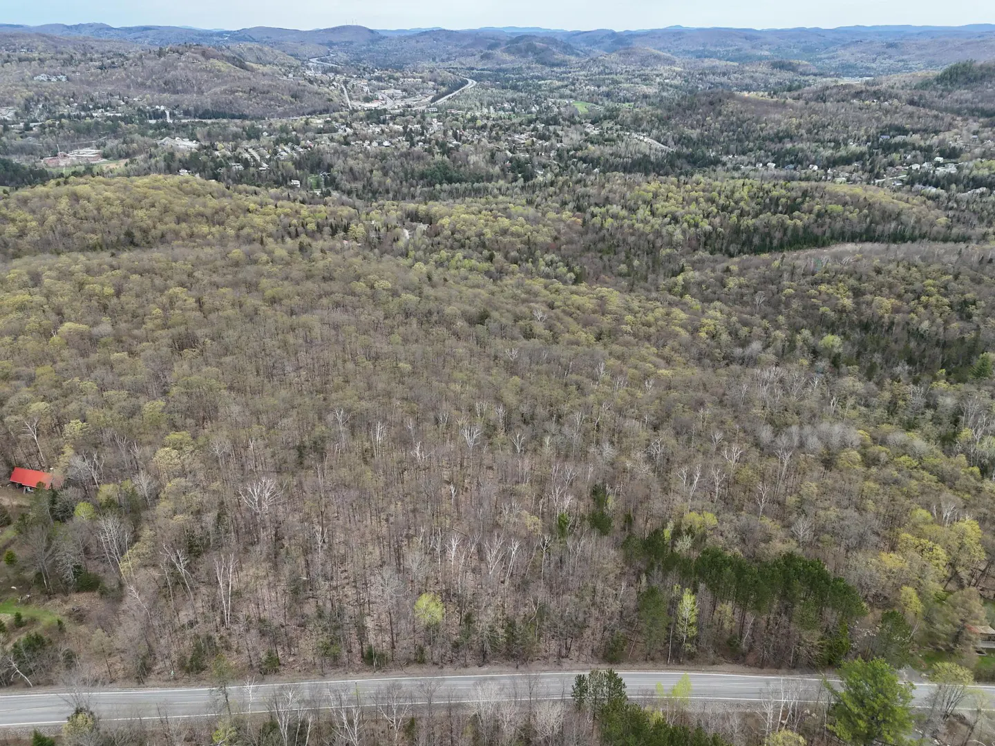 Aerial view of wooded land with a road in the foreground and a town in the distance.