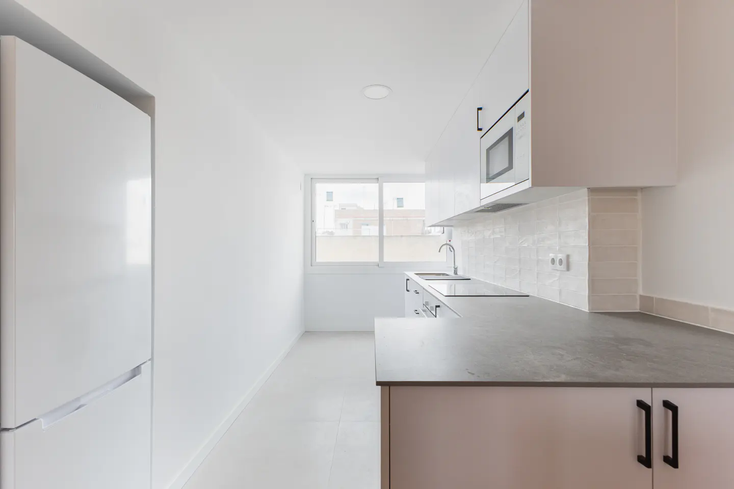 Bright, modern kitchen with white cabinets, gray countertops, and stainless steel appliances. A window provides natural light.