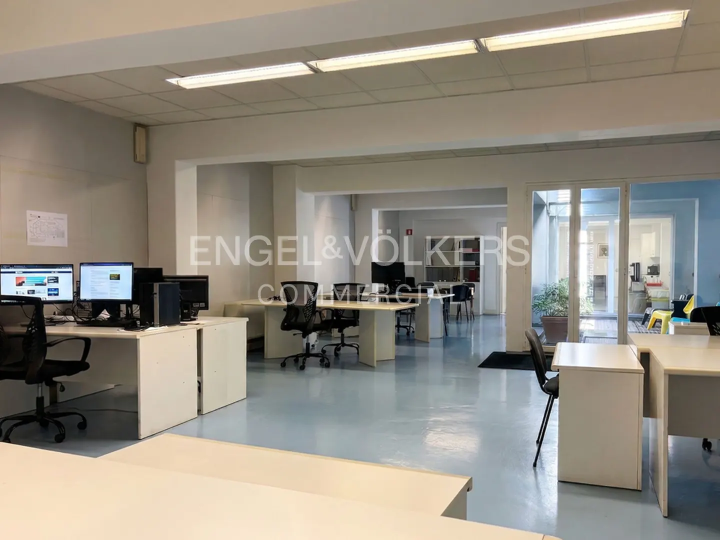 Bright, open office space with white desks, black chairs, and computer setups. Engel & Völkers logo visible in the background.