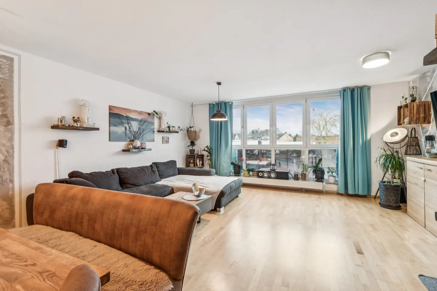 Bright living room with hardwood floors, a gray sectional sofa, and large windows with blue curtains.