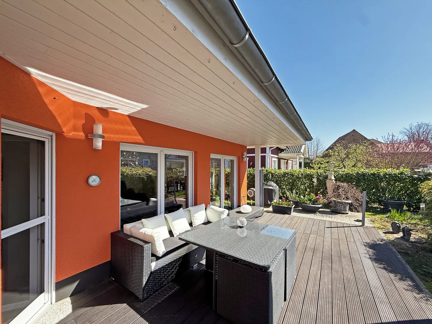 Outdoor patio with dark wicker furniture, white cushions, and an orange house wall under a white roof.