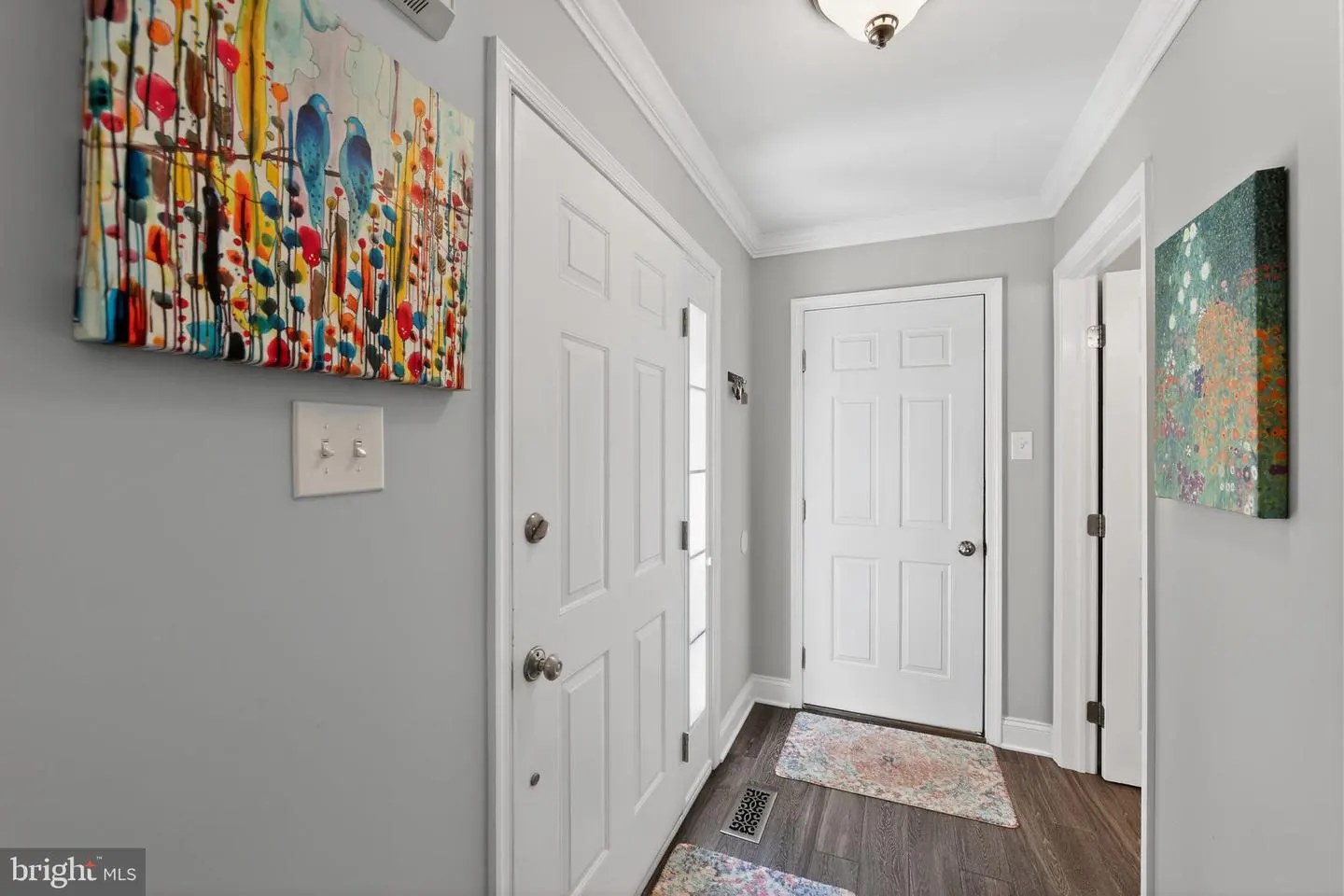 Hallway with gray walls, white trim, and dark wood floors. Two white doors, colorful art, and a light fixture are visible.