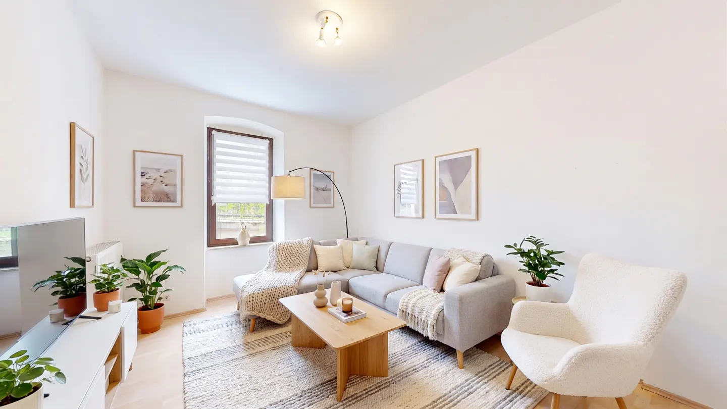 Bright living room with a gray sectional sofa, a wooden coffee table, and a white armchair on a striped rug. Art adorns the white walls.