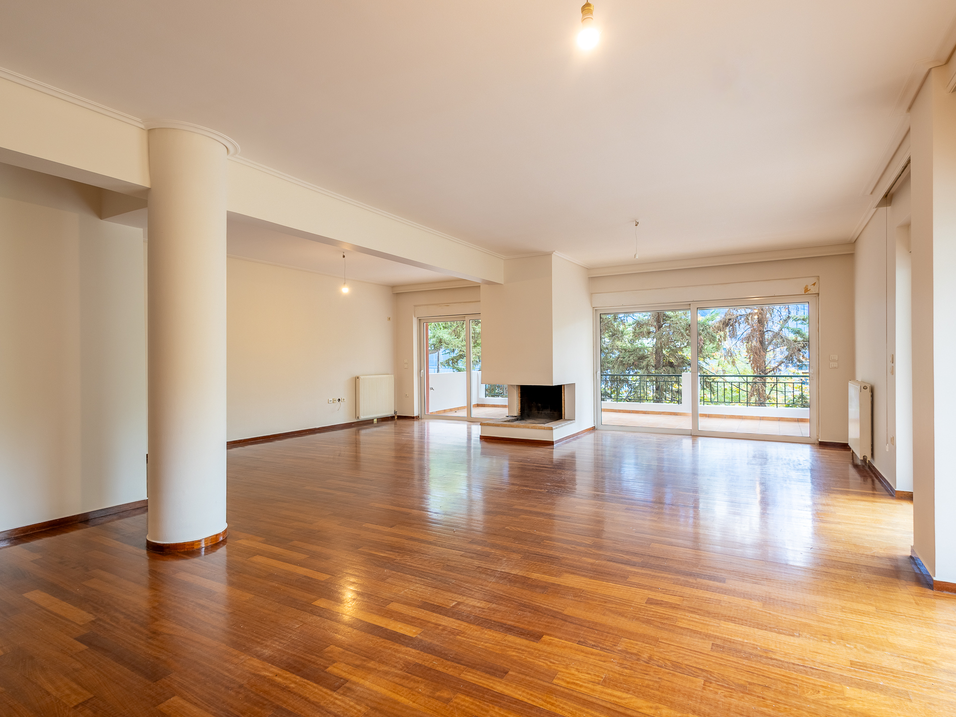 Spacious, empty living room with polished hardwood floors, a central fireplace, and large glass doors leading to a balcony. [AI-generated text]