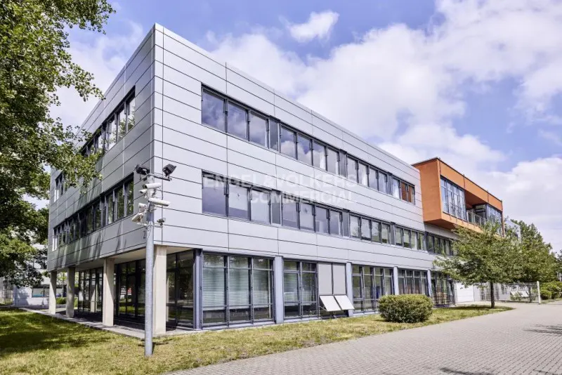 Exterior of a modern, three-story commercial building with silver panels and dark-framed windows under a partly cloudy sky.
