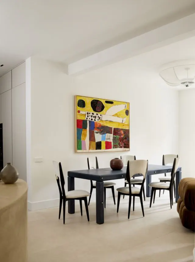 A bright dining room with a dark wood table and chairs, a colorful abstract painting on the wall, and light wood floors.