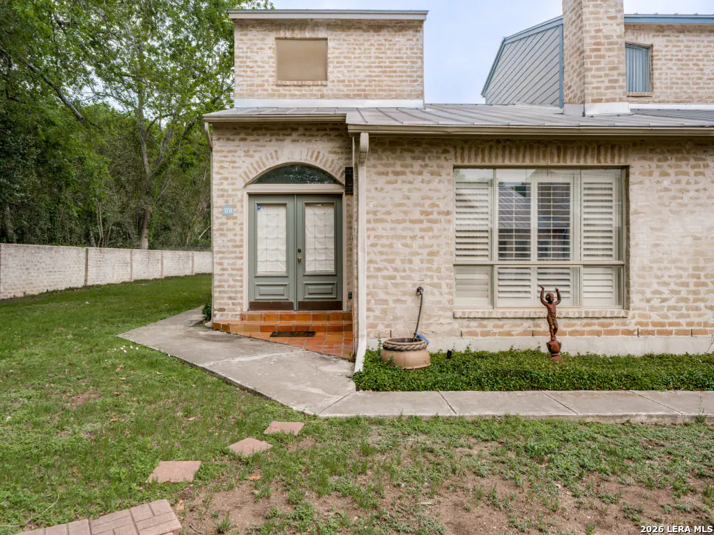 Exterior of a two-story beige brick house with a green lawn and a walkway to the arched double-door entrance.