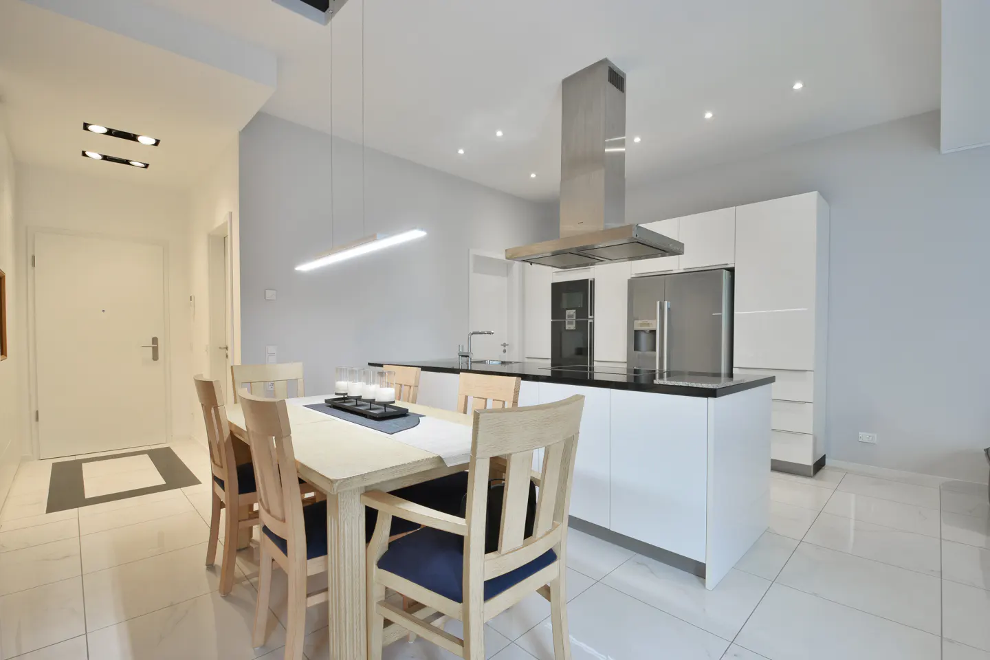 Bright, modern kitchen with a dining table. Stainless steel appliances and a black countertop island are visible. The chairs have blue cushions.