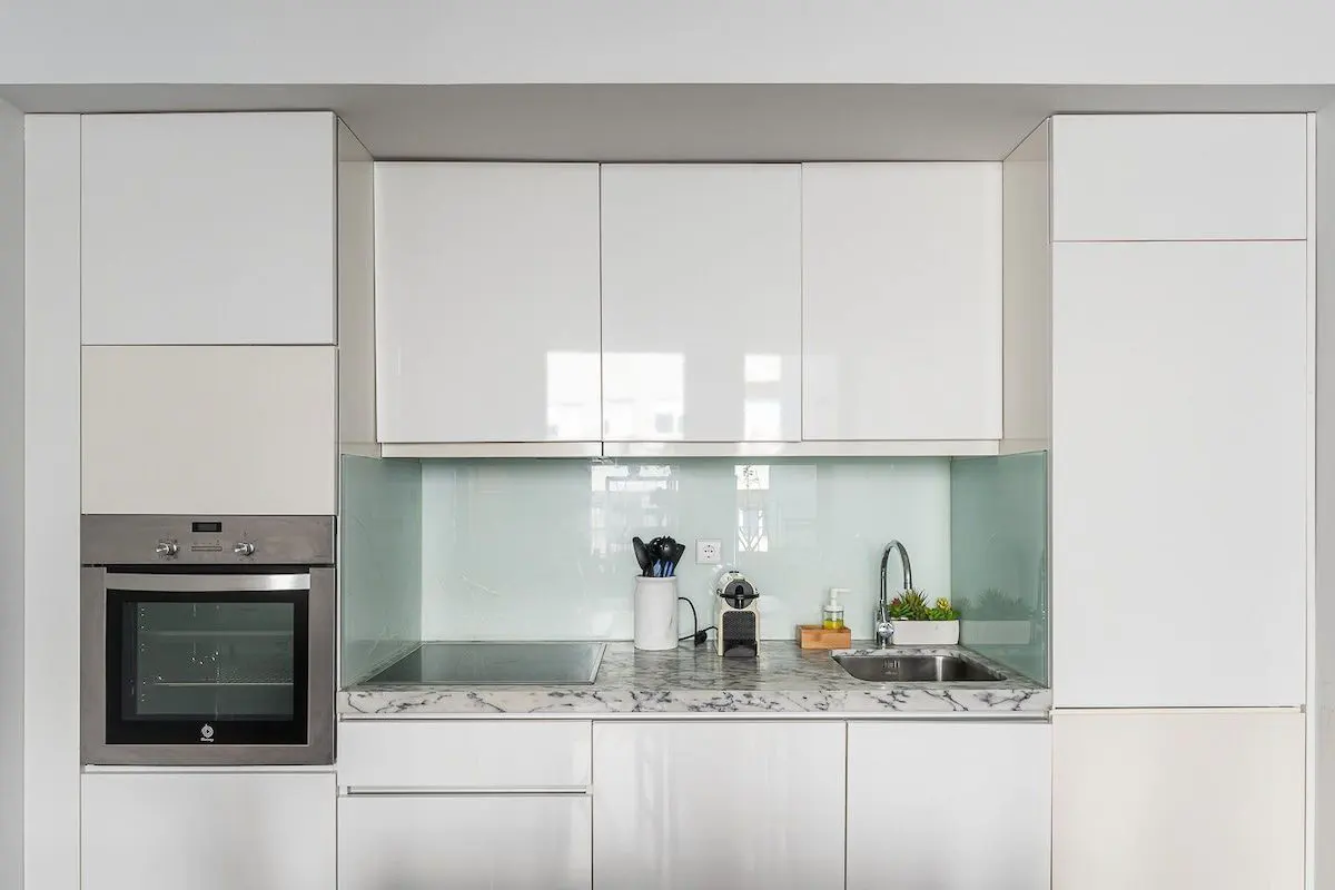 A modern kitchen with white cabinets, marble countertops, and stainless steel appliances.