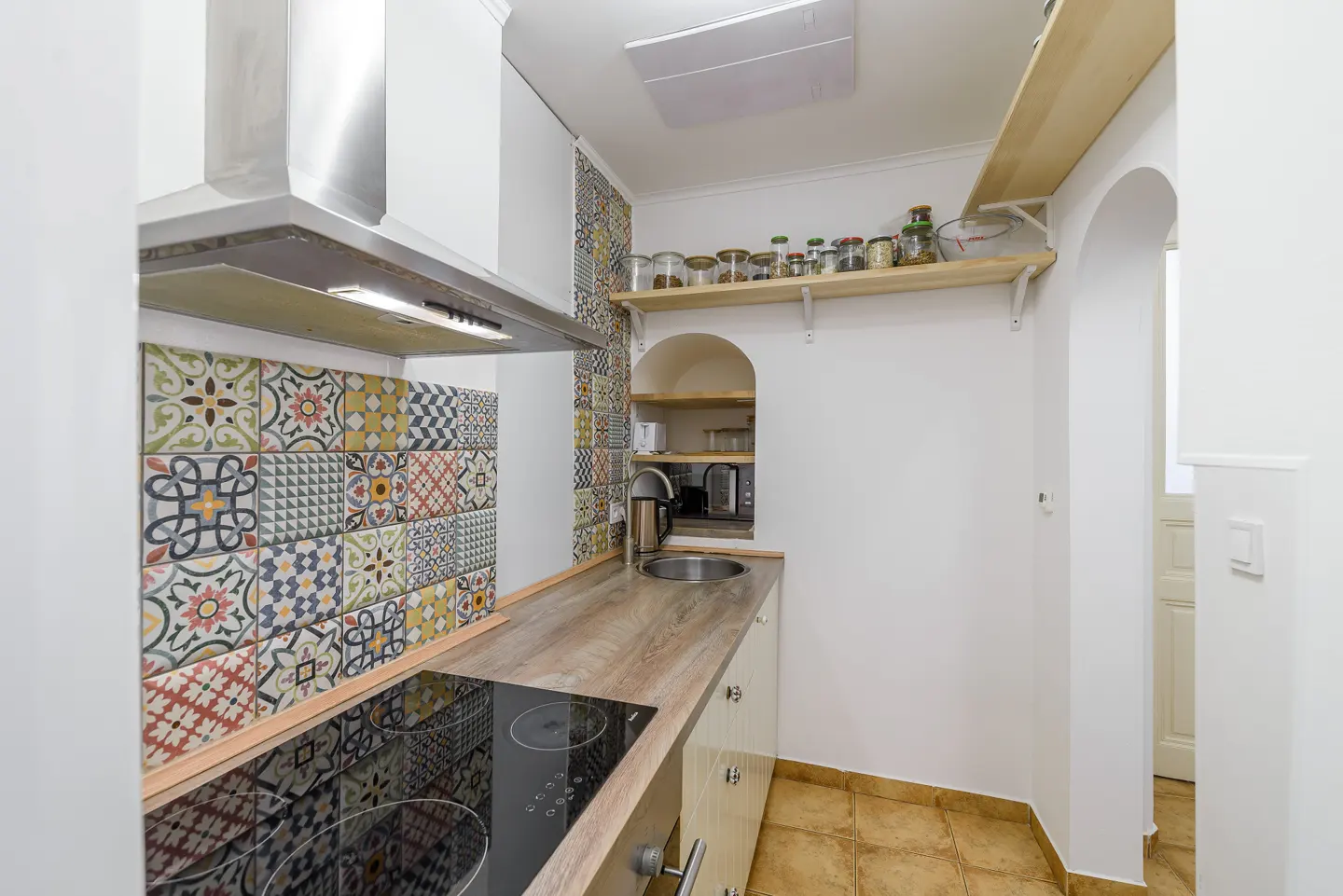 Modern kitchen with wood-look counters, colorful patterned tile backsplash, stainless steel stove, and open shelving.