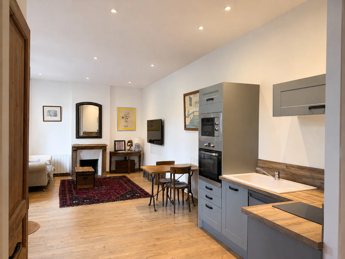 Open-plan living area with a grey kitchen, wooden dining table, and a cozy lounge space featuring a fireplace and rug.