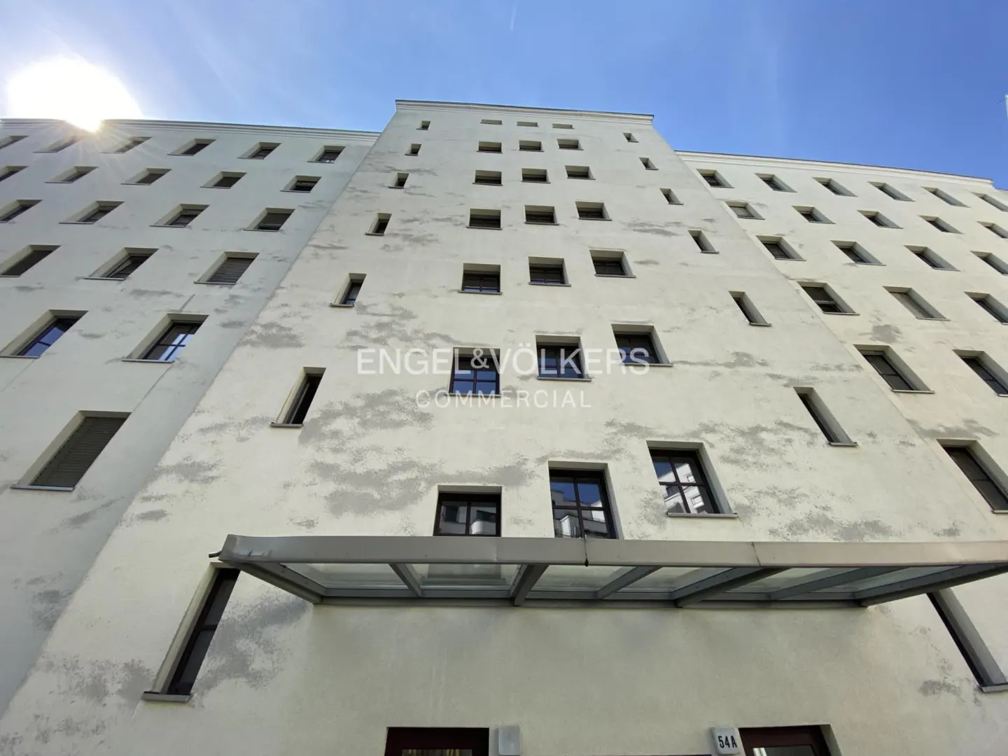 Exterior shot of a tall, white building with many windows under a blue sky. "Engel & Völkers Commercial" logo is visible.