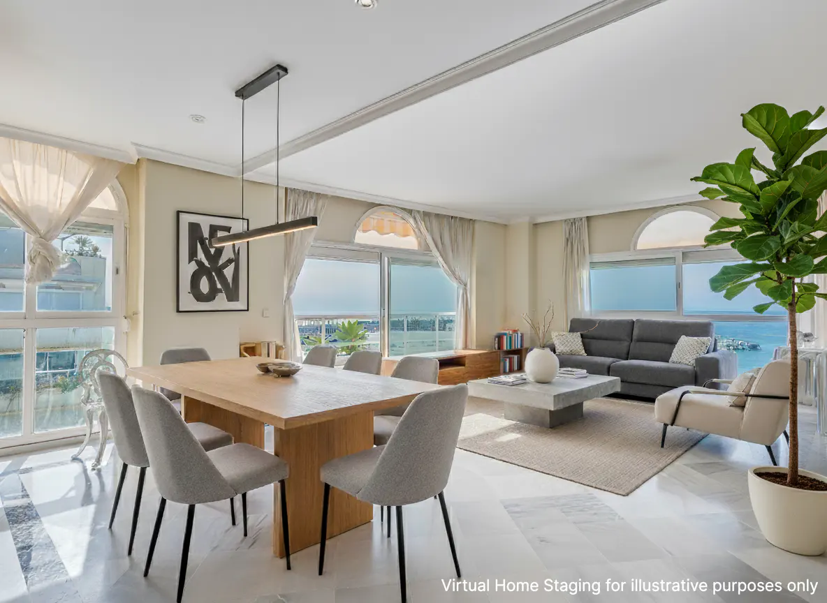 Bright, open-concept living and dining area with a wood table, gray chairs, and ocean views. A gray sofa and potted plant are visible.