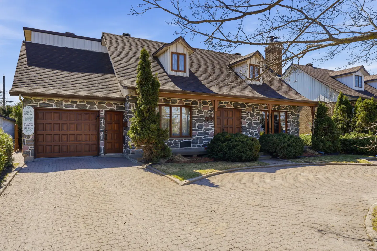 Exterior of a stone house with a brown roof, garage, and brick driveway.