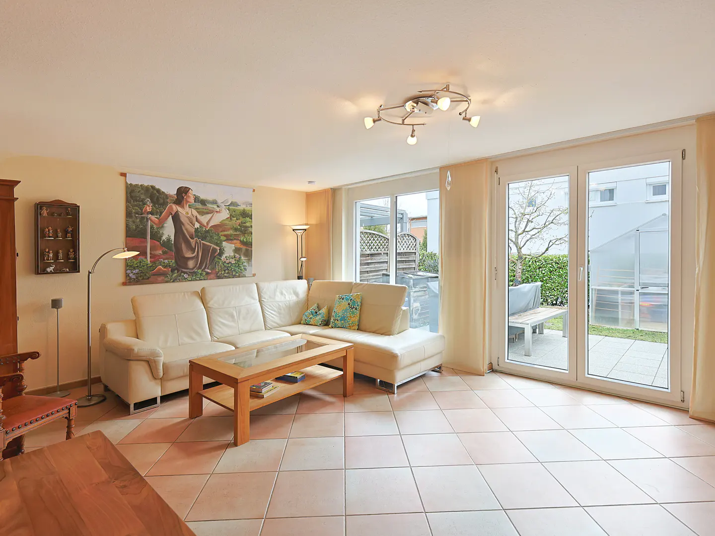 Living room with a white sectional sofa, wood coffee table, and a large tapestry on the wall. Patio doors lead to an outdoor area.