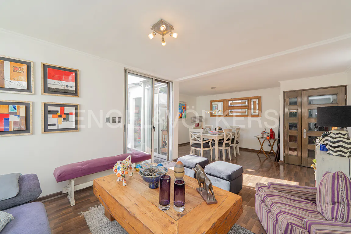 Living room with a wooden coffee table, purple bench, striped armchair, and dining area visible in the background.