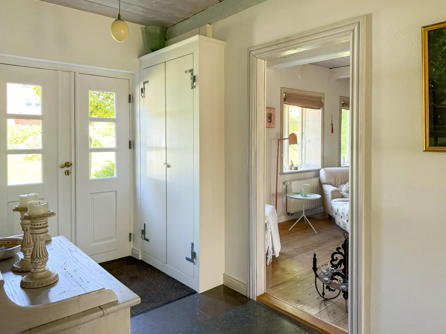 Entryway with white doors, a tall white cabinet, and a glimpse into a living room with a floral sofa and wooden floors.