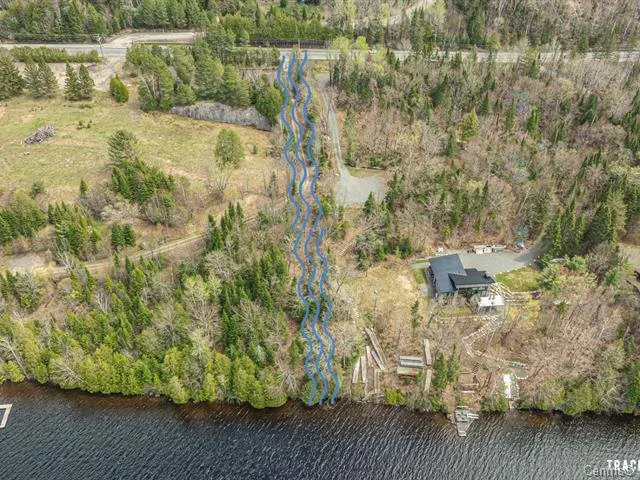 Aerial view of a lakefront property with a modern house, surrounded by lush green trees and a winding blue stream.