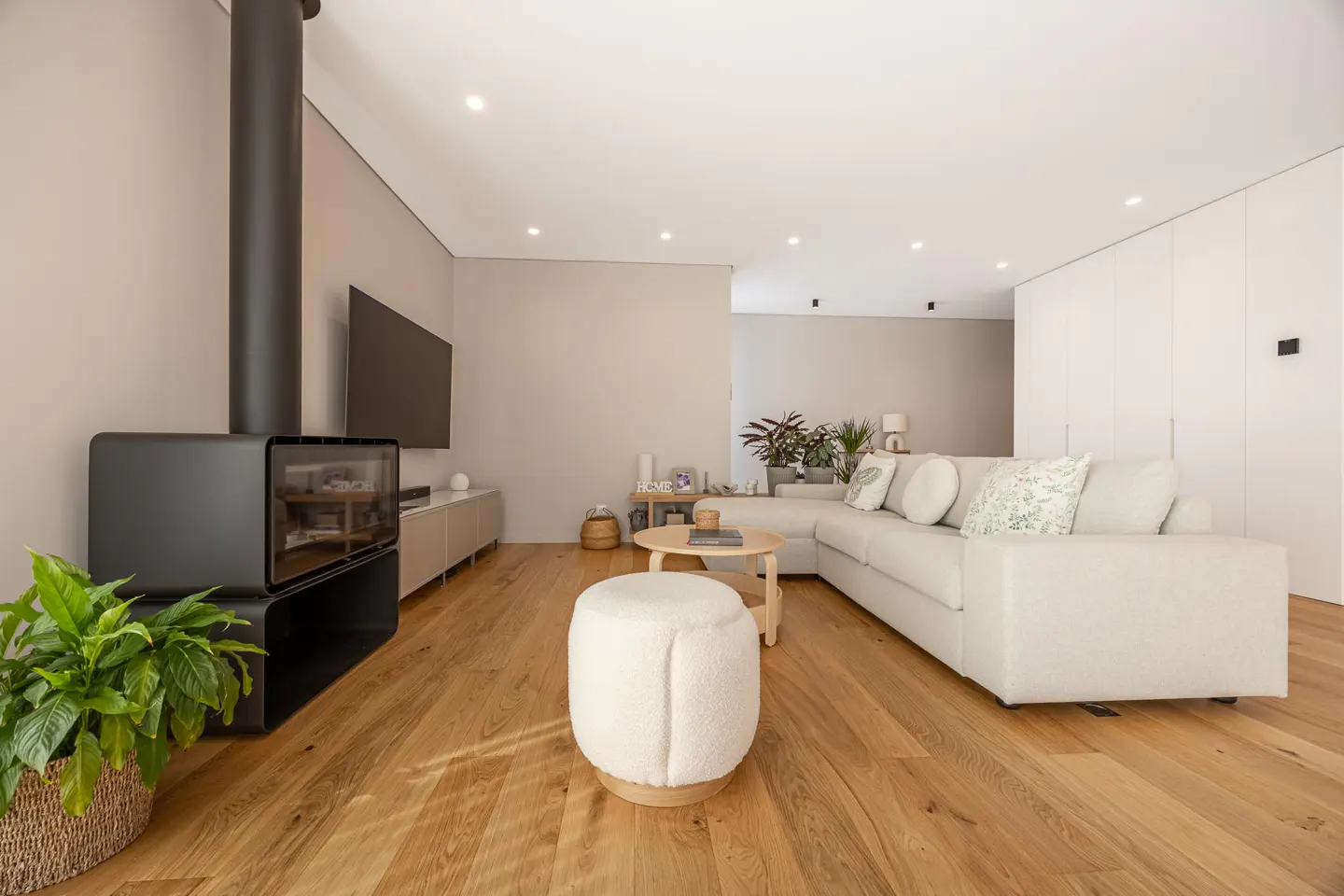Bright living room with hardwood floors, a white sectional sofa, a black fireplace, and a round wooden coffee table.