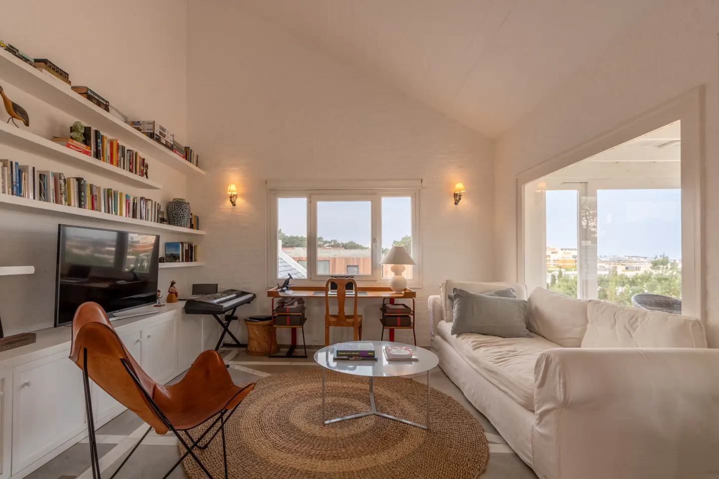 Bright living room with white walls, a white sofa, a brown leather butterfly chair, a round rug, and built-in bookshelves.
