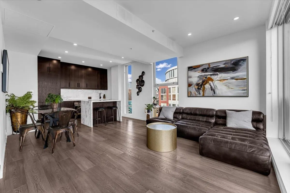 Open-concept living space with dark wood floors, a brown leather sofa, and a kitchen with dark cabinets.