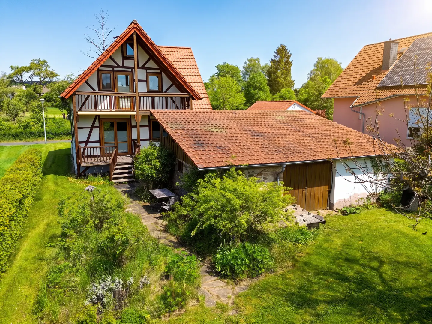 Two-story timber frame house with a red tile roof and a green lawn. A table and chairs sit on a stone patio.