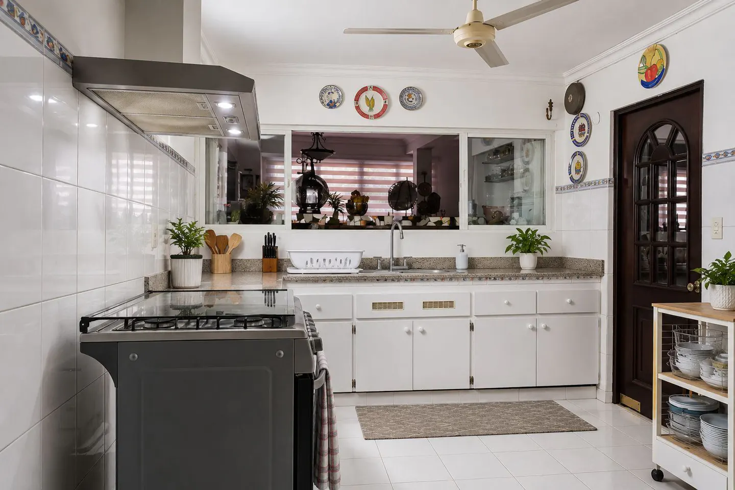Bright kitchen with white cabinets, granite countertops, and white tiled walls. A gray stove sits to the left, and a dark wood door is on the right.