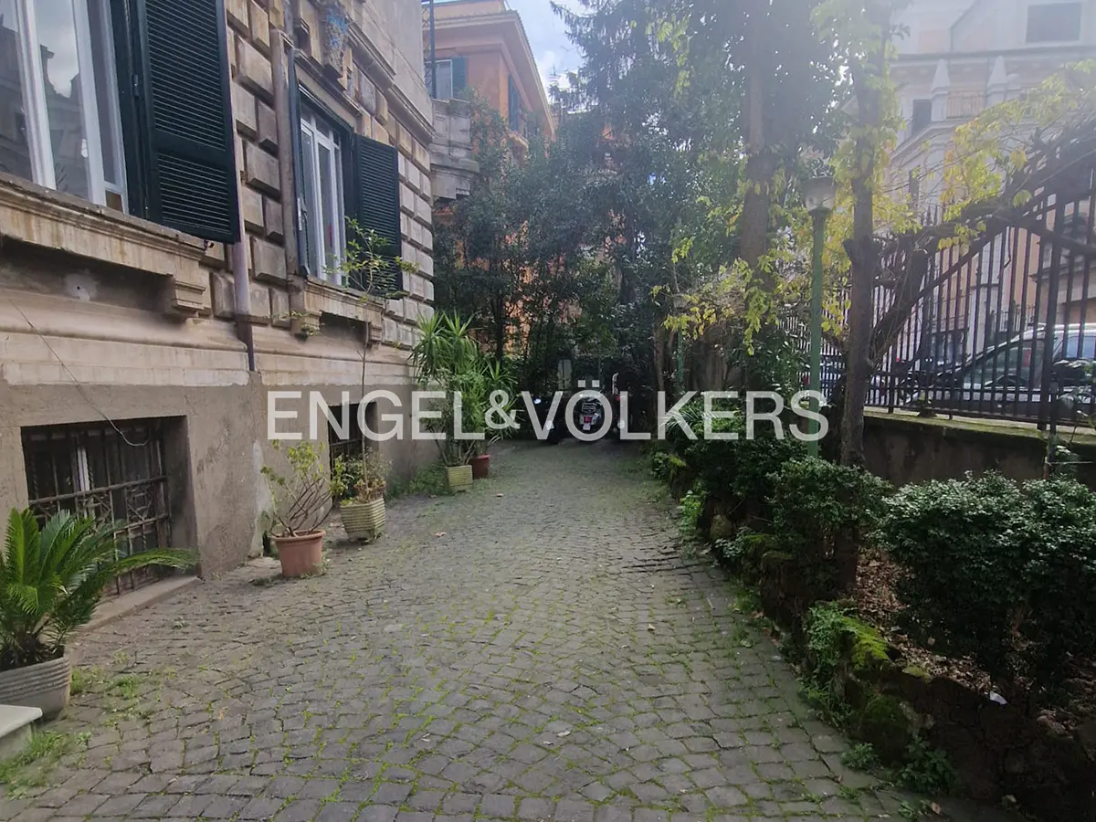 Exterior view of a stone driveway leading to a building with green shutters and the Engel & Völkers logo.