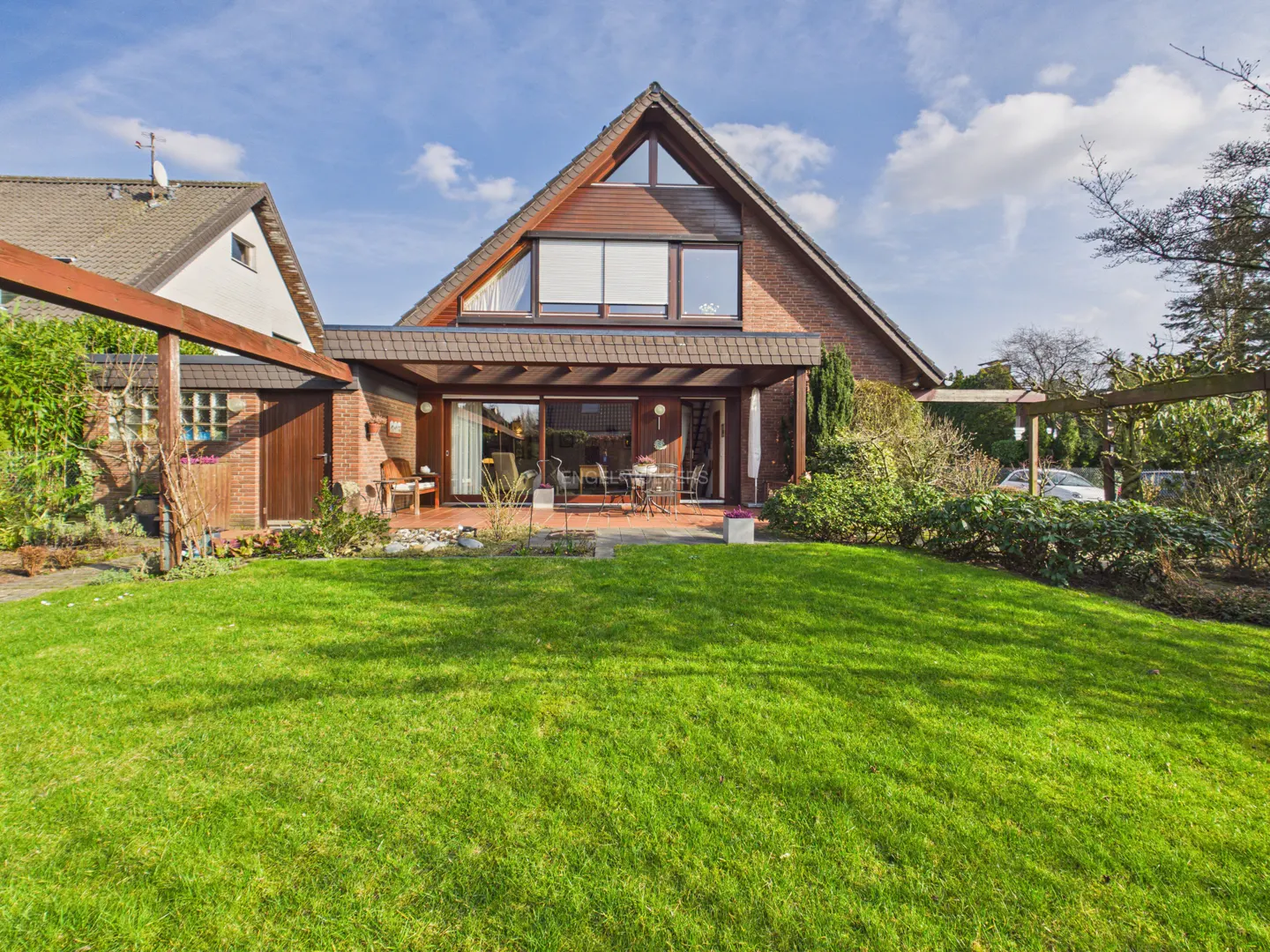 A brick house with a triangular roof and a green lawn under a blue sky.