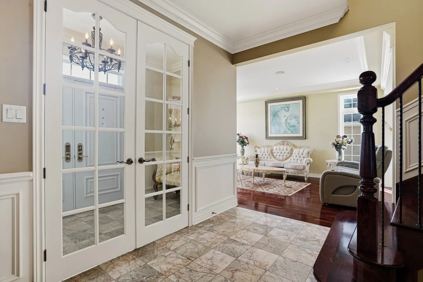 Foyer with marble tile floor, white french doors, and a glimpse into a living room with a sofa and artwork.