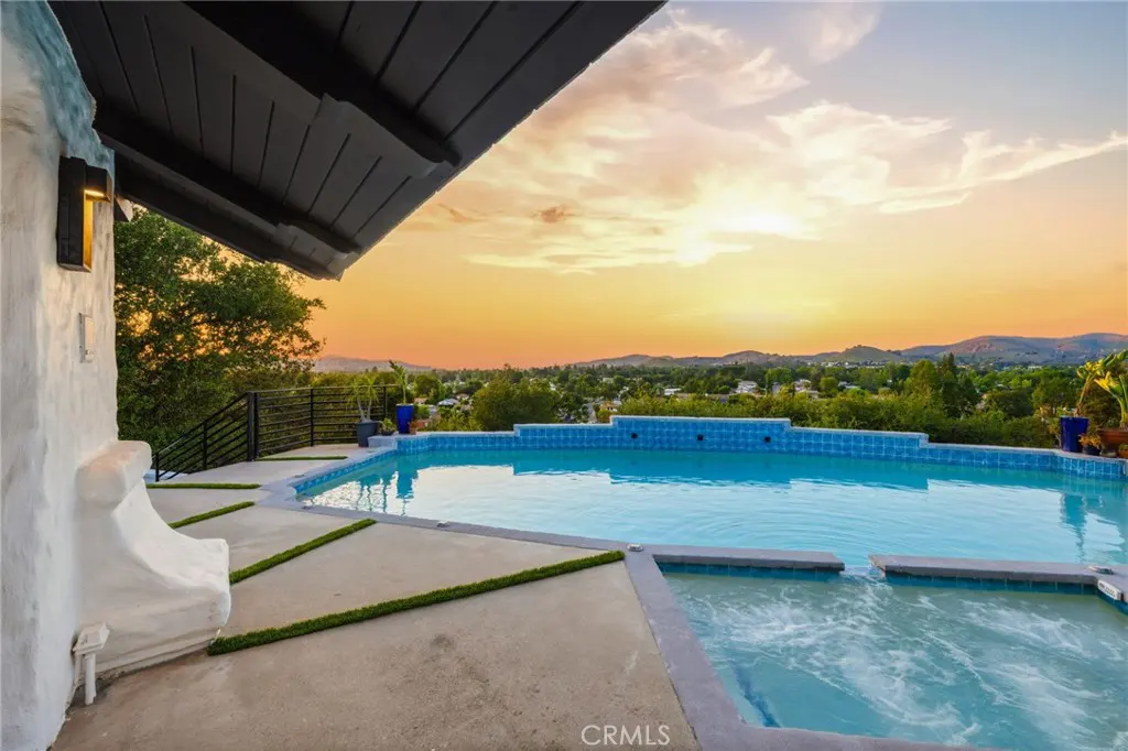 Outdoor pool and jacuzzi with blue tiles, concrete patio, and sunset view.