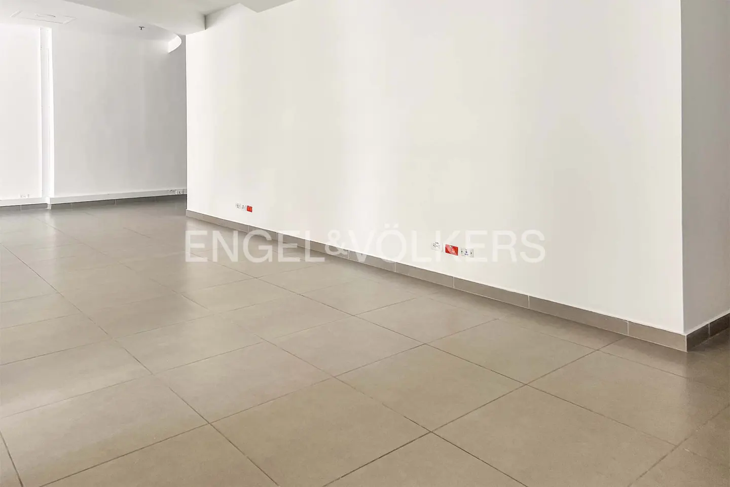 Empty room with beige tile floor and white walls. Red electrical outlets are visible along the base of the wall.