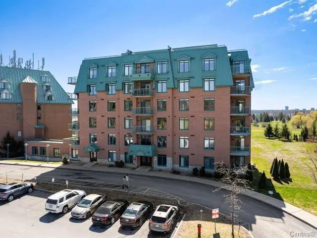 Exterior view of a multi-story brick apartment building with a green metal roof, balconies, and a parking lot in front.
