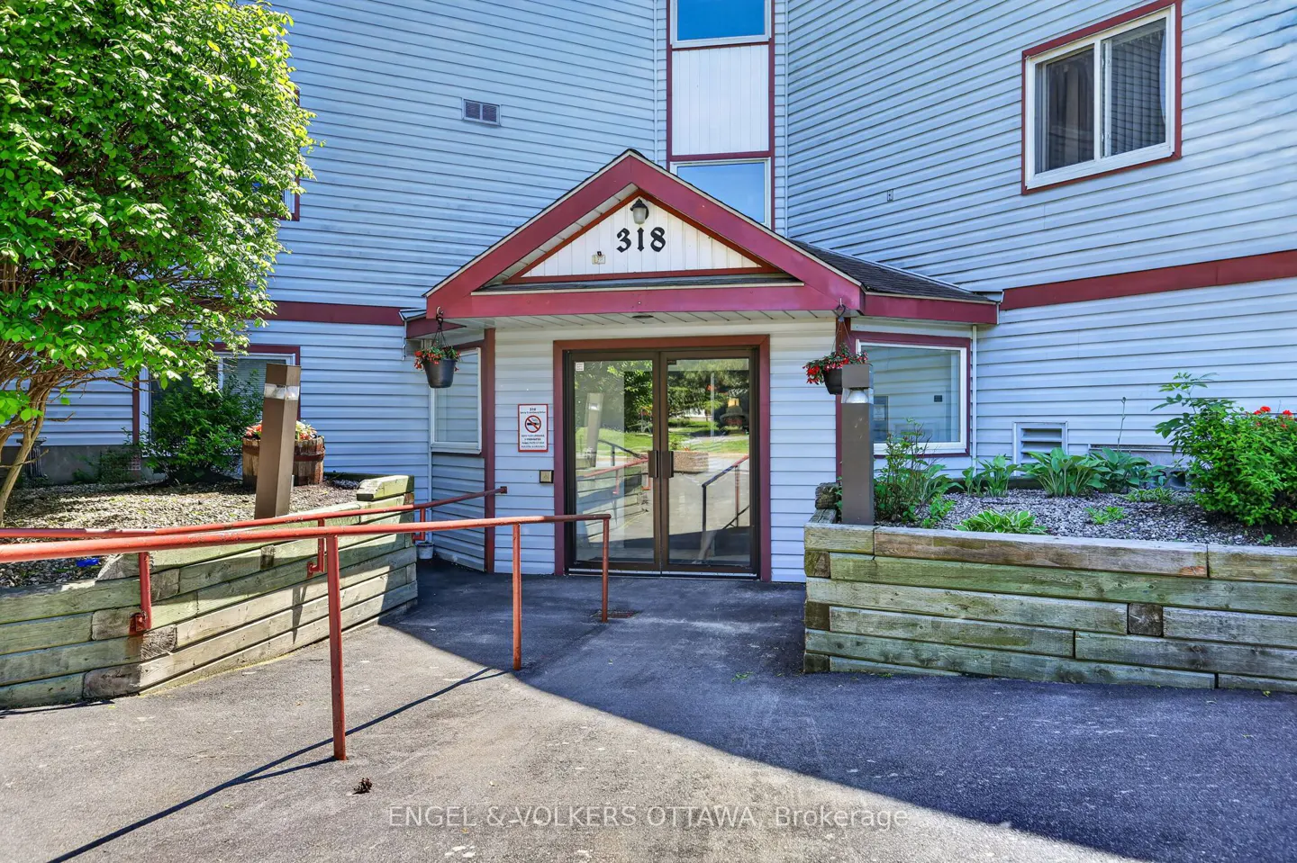 Entrance to a light blue building with number 318, a red-trimmed porch, glass doors, and a red metal wheelchair ramp.