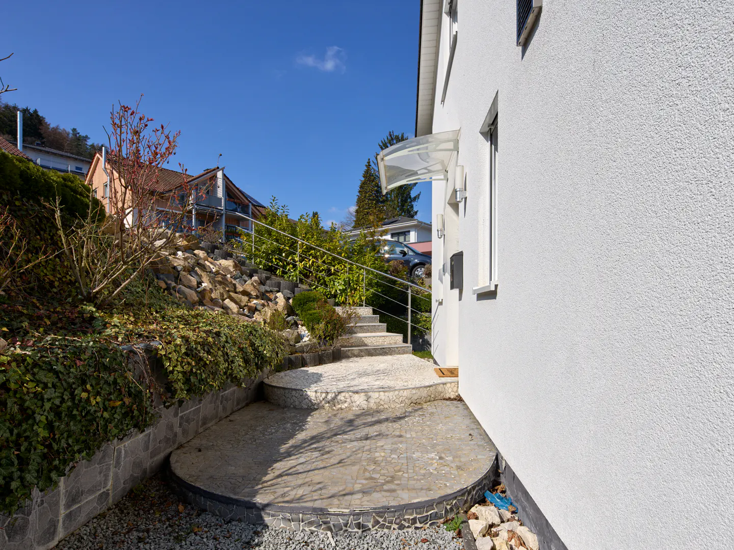 Exterior view of a white house with stone steps and a metal railing leading to the front door. A clear awning covers the entrance.