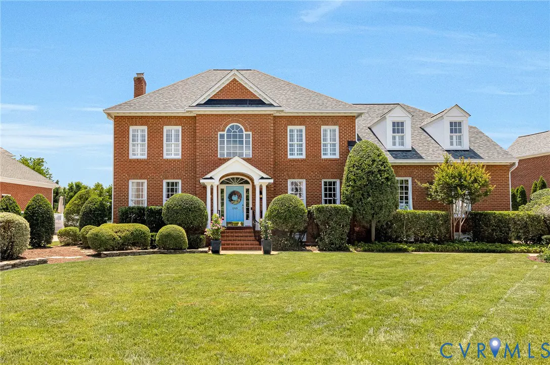 Two-story brick house with a blue front door and manicured lawn under a clear blue sky.