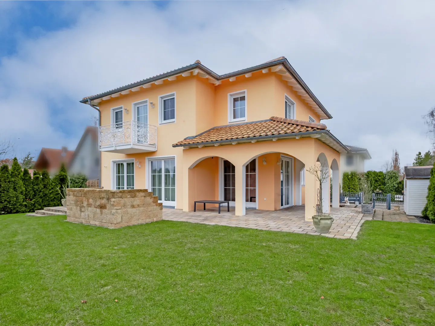 Two-story peach house with a red tile roof, white trim, and a green lawn. A stone wall and patio are visible.