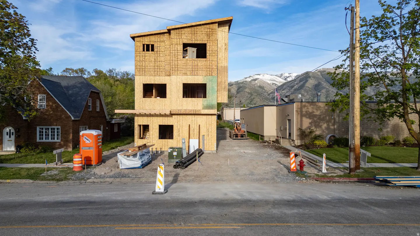 A three-story wood-framed house under construction, with mountains in the background.