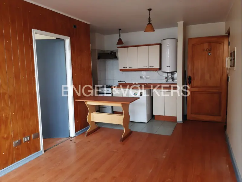 A wide shot of a studio apartment with wood floors, a small kitchen, and a table.