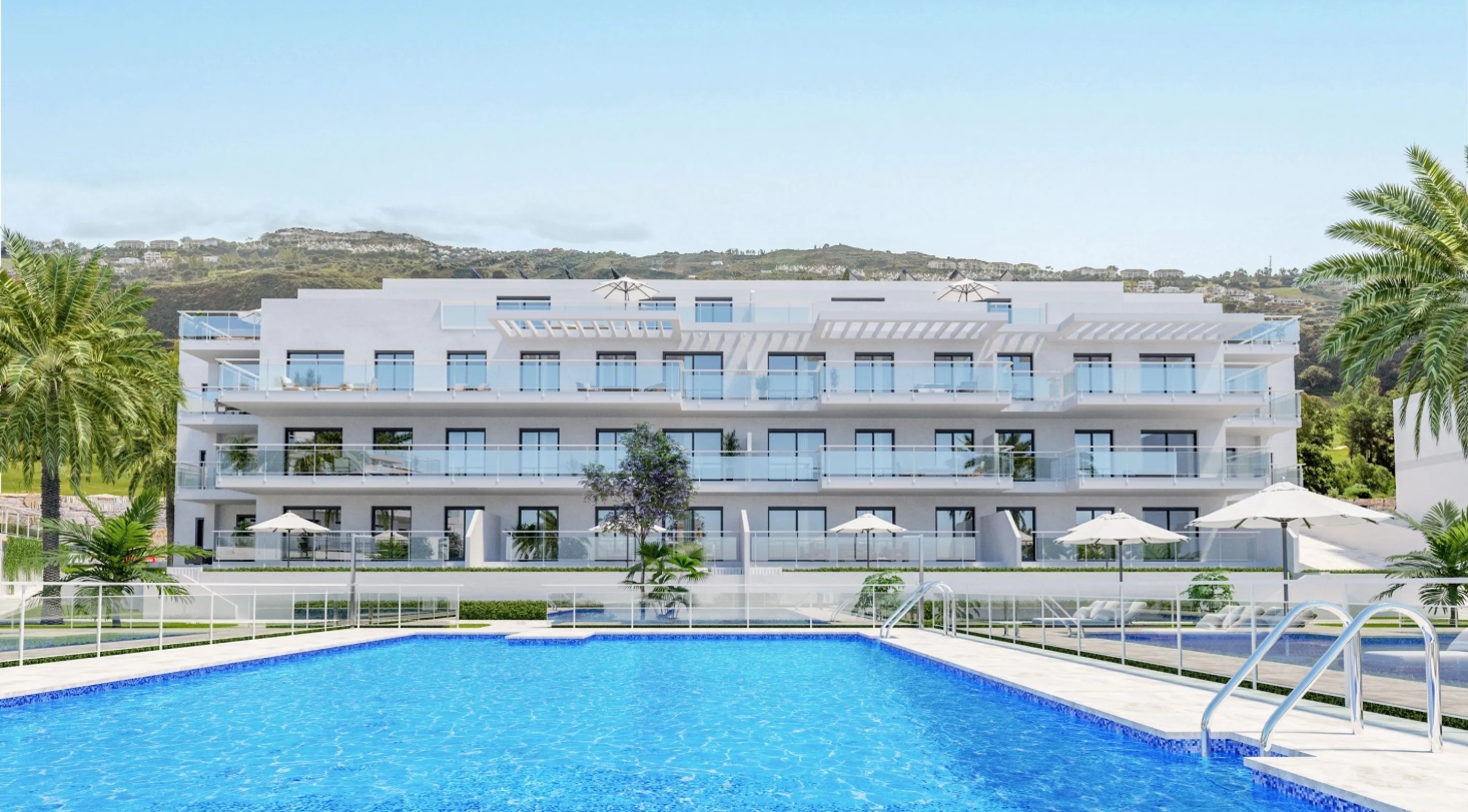 Modern white apartment building with balconies overlooking a blue swimming pool, palm trees, and distant hills.