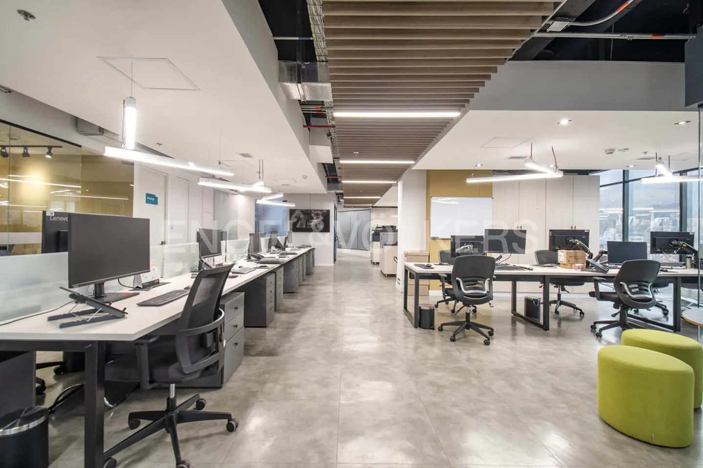 Bright, modern office space with rows of desks, computers, and ergonomic chairs. Green ottomans add a pop of color.