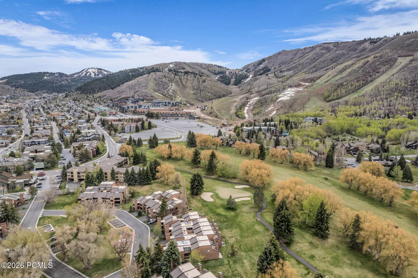 Aerial view of condos near a golf course and ski mountain under a blue sky with scattered clouds.