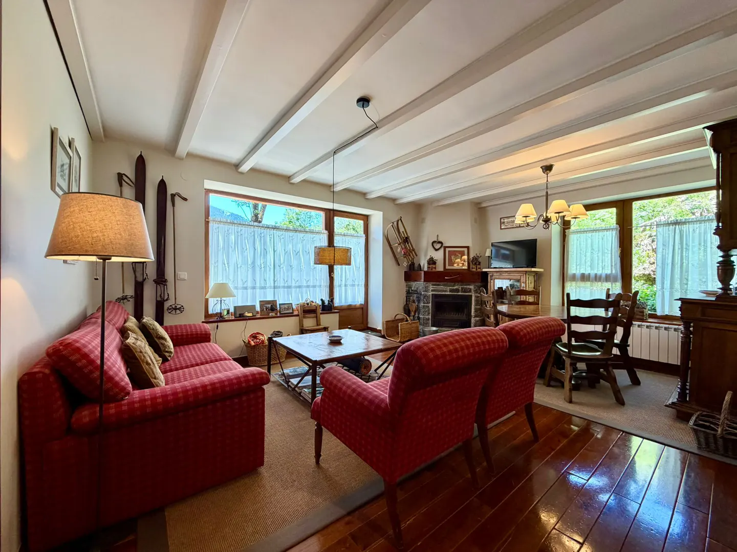 Cozy living room with red plaid sofa and chairs, fireplace, wood floors, and beamed ceiling. Skis hang on the wall.