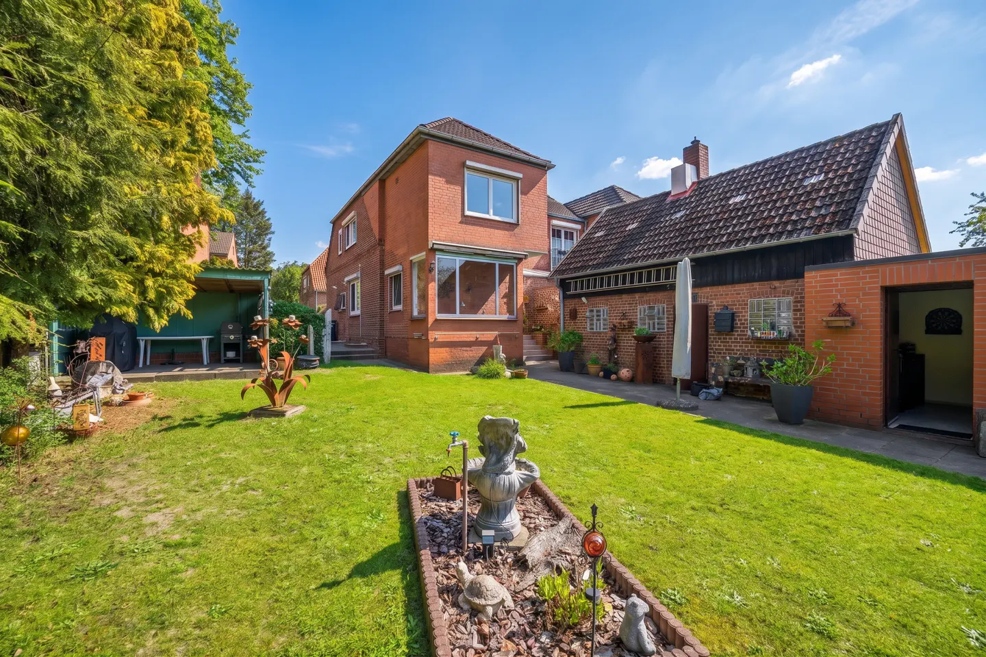 A lush green lawn with garden art in the backyard of a brick house under a blue sky.