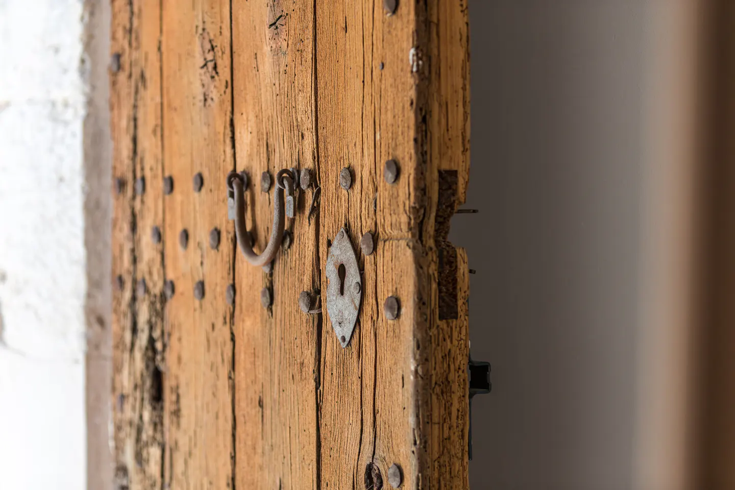 Close-up of a weathered, light-brown wooden door with metal accents, including a handle, keyhole, and decorative studs.